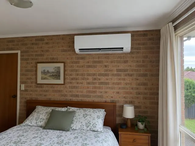 Bedroom with a wall-mounted split system above a bed, brick wall and window curtains in Valley View