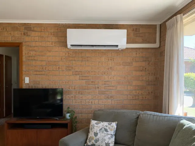 Wall-mounted split system on a brick living room wall above a TV and sofa in Gilles Plains